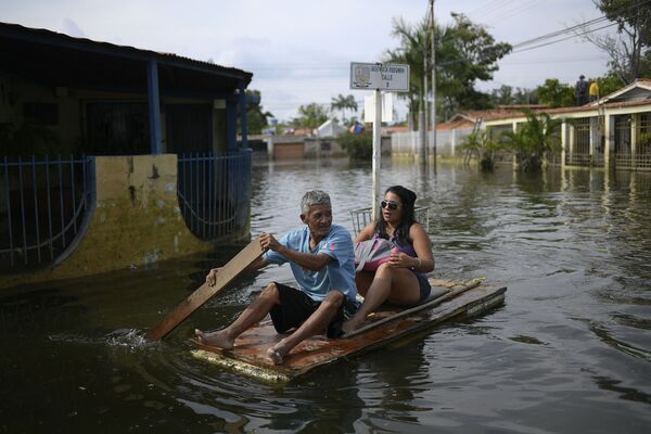 大雨による洪水に見舞われたベネズエラ中北部アラグア州で、扉をいかだにして冠水した道路を渡る住民 - Sputnik 日本