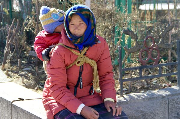 中国・チベット自治区ラサ市で、幼児を背負って通りを歩く女性 - Sputnik 日本