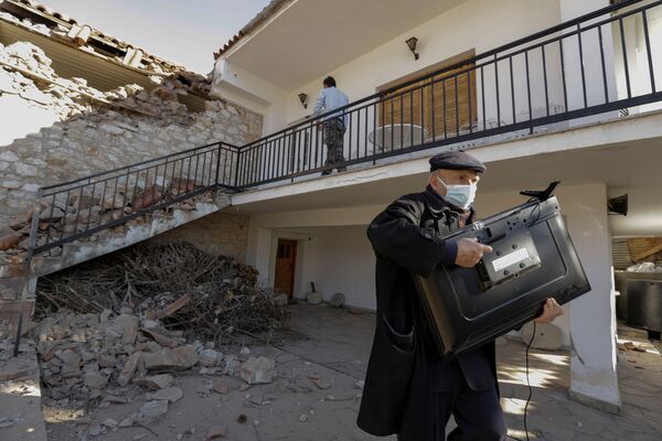 ギリシャ中部のダマシ村で、地震の被害を受けた家屋からテレビを運ぶ男性 - Sputnik 日本