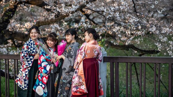 Девушки в традиционной для выпускных церемоний в университете одежде, позируют под цветущей сакурой в парке Китаномару в Токио, Япония - Sputnik 日本