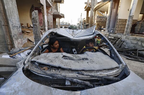 パレスチナ自治区ガザ地区で、イスラエル軍とイスラム過激派組織「ハマス」の衝突で破壊された車の中で遊ぶ子どもたち - Sputnik 日本