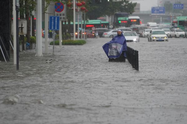 河南省の州都・鄭州市で、冠水した道路にレインコートを着て立つ市民 - Sputnik 日本