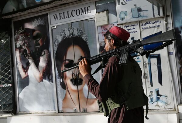 アフガニスタン・カブールで、スプレーで落書きがされた女性のポスターの前を通るタリバン戦闘員 - Sputnik 日本