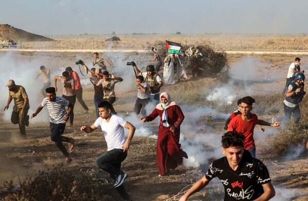 パレスチナ自治区ガザ地区の国境沿いで行われた抗議デモで、イスラエル治安部隊が発射した催涙ガスから逃げるデモ隊とジャーナリストら - Sputnik 日本