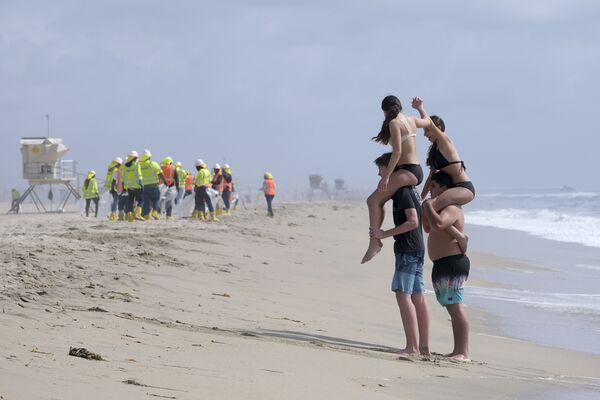 米カリフォルニア州ハンティントンビーチで、作業員が原油で汚染されたビーチの清掃をする中、海水浴に訪れた人々 - Sputnik 日本