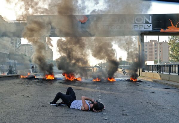 抗議デモの最中、炎上するタイヤに塞がれた道路に横たわるデモ参加者（レバノン・ベイルート、29日） - Sputnik 日本
