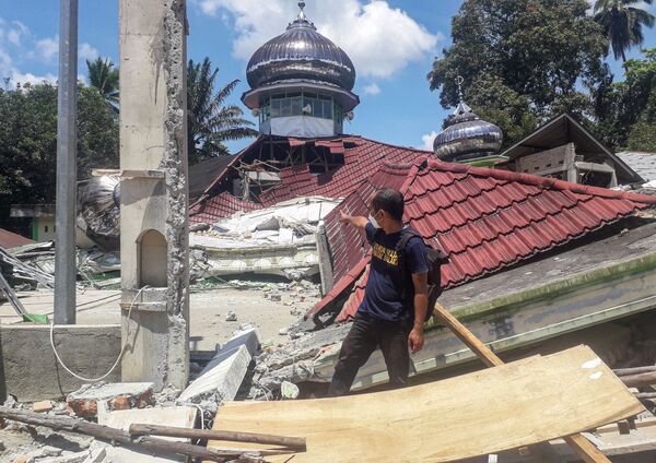 地震で倒壊したモスクの前にを歩く男性（インドネシア・西スマトラ州西パサマン県、25日） - Sputnik 日本