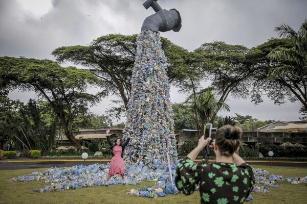 国連環境計画（UNEP）本部で開催された国連環境総会（UNEA）で、蛇口から流れ出るペットボトルをかたどった巨大オブジェの前で写真を撮る代表者ら（ケニア・ナイロビ、2日） - Sputnik 日本
