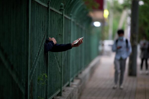 ロックダウンが行われている地域で、フェンス越しに手を伸ばしてスマートフォンを捜査する住民（中国・北京、27日） - Sputnik 日本