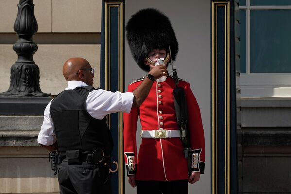 バッキンガム宮殿の警備にあたる衛兵に水を含ませる警察官（英ロンドン、18日） - Sputnik 日本
