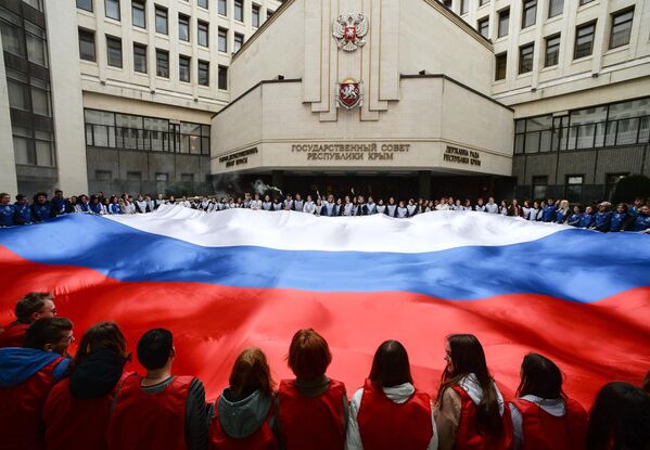 クリミア国家評議会前で行われたクリミアのロシア再編入を記念する集会で、巨大なロシア国旗を広げる参加者（ロシア・クリミア共和国、11日） - Sputnik 日本
