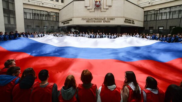 クリミア国家評議会前で行われたクリミアのロシア再編入を記念する集会で、巨大なロシア国旗を広げる参加者（ロシア・クリミア共和国、11日） - Sputnik 日本