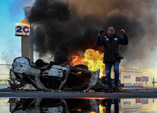 マルセイユ港で、横転し燃える車の前に立つ労働組合の男性（フランス・マルセイユ、22日） - Sputnik 日本