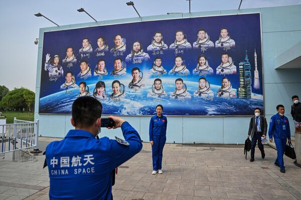 酒泉衛星発射センターで、宇宙飛行士が描かれた看板の前で記念撮影をする中国国家航天局の職員（中国・甘粛省、30日） - Sputnik 日本