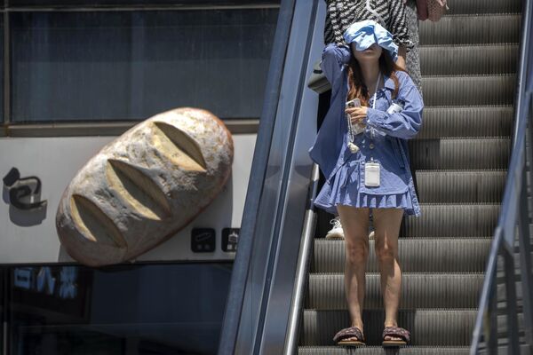 布で日差しを遮って商業施設のエスカレーターに乗る女性（中国・北京、7日） - Sputnik 日本