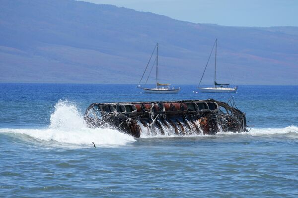 ラハイナ沖で、焼け焦げたボートに打ち寄せる波（ハワイ州・マウイ島、12日） - Sputnik 日本