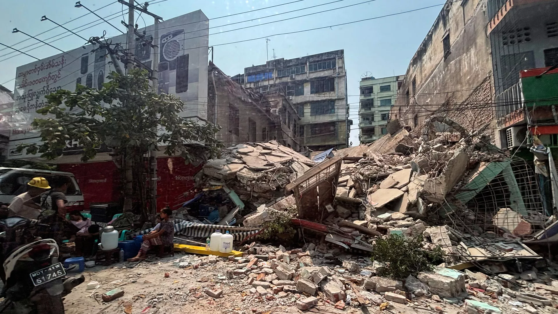 Local residents rest near a damaged building in the aftermath of an earthquake, in Mandalay, central Myanmar, Sunday, March 30, 2025. 