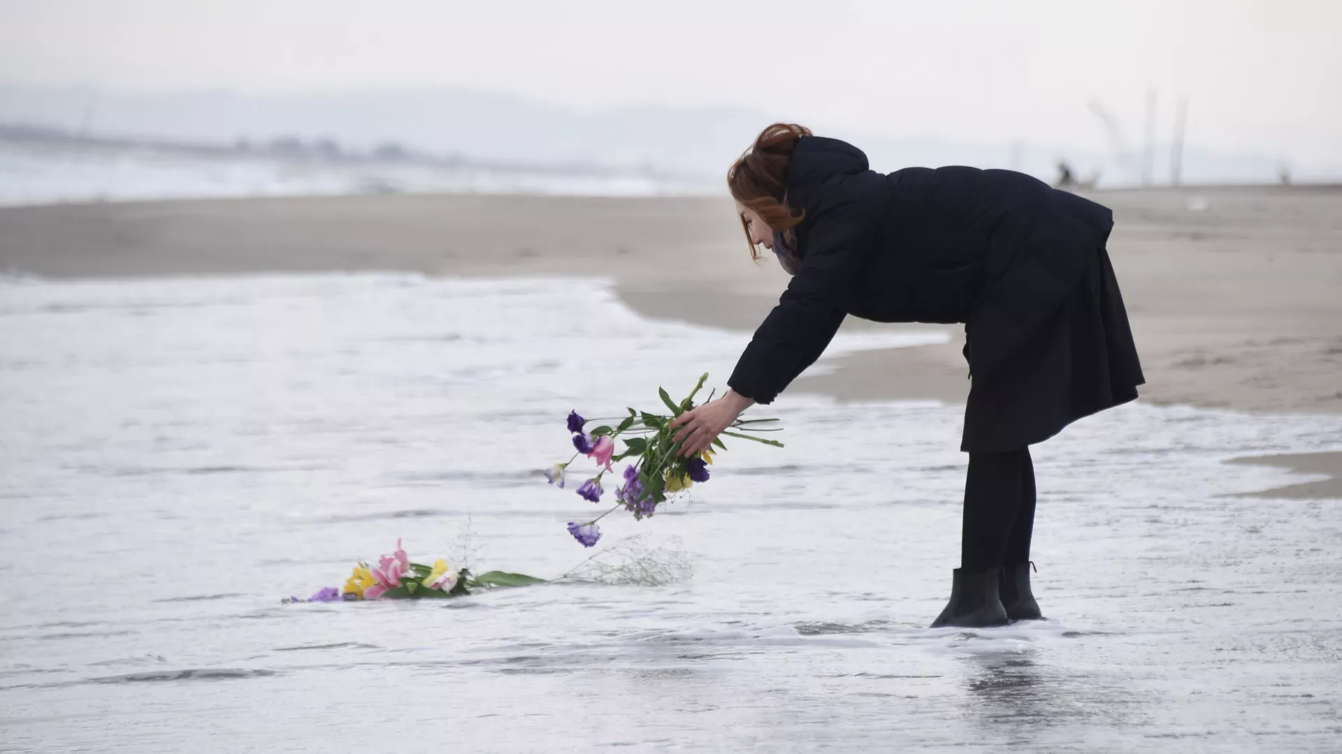 津波の犠牲者の追悼のため水に花を投げ入れる女性
