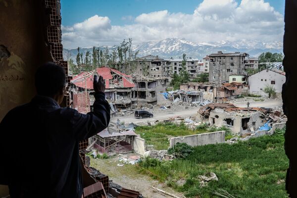 トルコのユクセコワ市、トルコ軍とクルド軍間の衝突で破壊された建物の前のバルコニーに立つ男 - Sputnik 日本