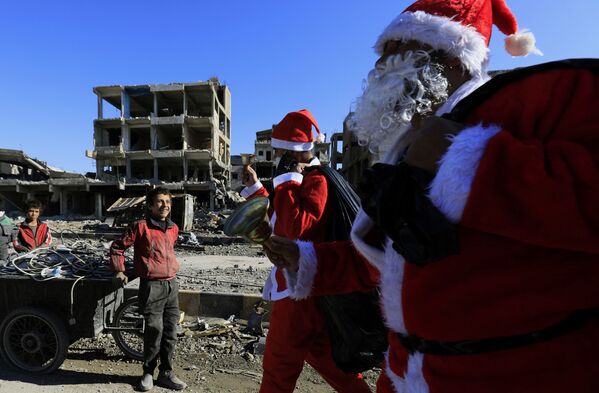 シリア・ラッカで、サンタクロースの格好をして通り過ぎる男性たちに笑いかける少年 - Sputnik 日本