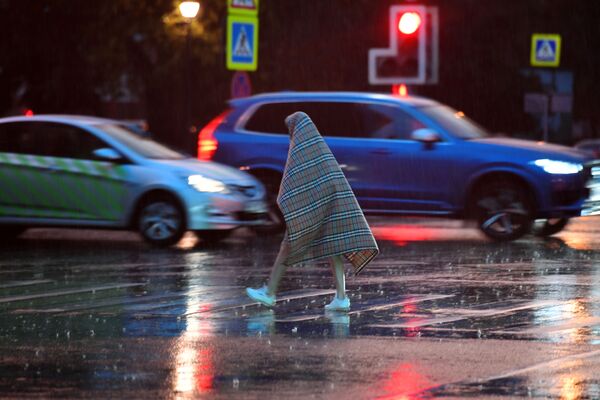 モスクワで強い雨が降る中、格子縞の肩掛けをかぶって、道路を横切る通行人 - Sputnik 日本