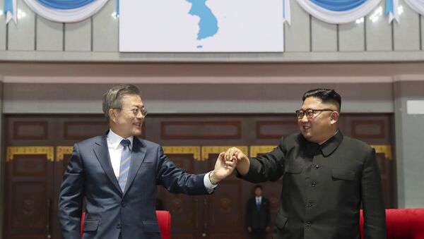 South Korean President Moon Jae-in, left, and North Korean leader Kim Jong Un hold their hands after watching the mass games performance of The Glorious Country at May Day Stadium in Pyongyang, North Korea, Wednesday, Sept. 19, 2018. Unification flag symbol at top centre. - Sputnik 日本
