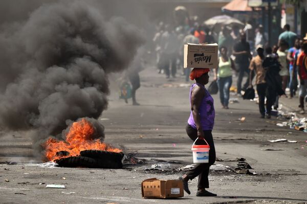 ハイチの首都ポルトープランスで、路上で燃えるタイヤのそばを通り過ぎる女性 - Sputnik 日本