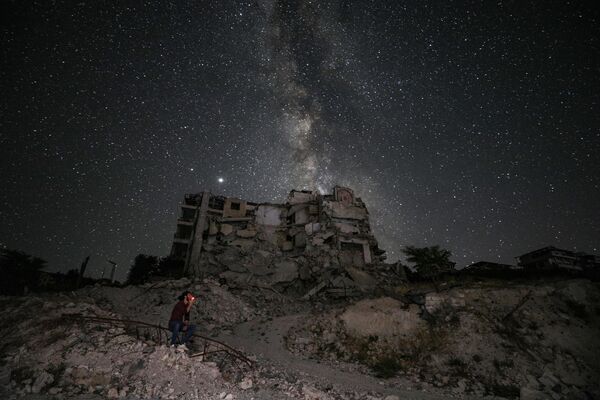 天の川が見える夜空と、爆撃で破壊された建物の前でタバコを吸う男性（シリア、イドリブ） - Sputnik 日本